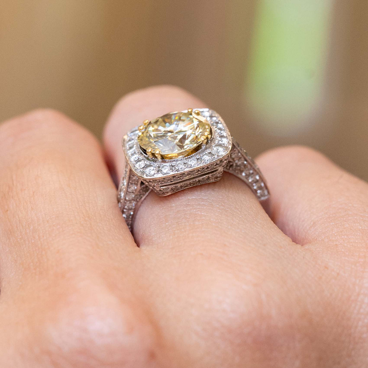 A close-up of a hand wearing a Vintage, 1990s yellow tinted diamond cluster engagement ring in white gold
