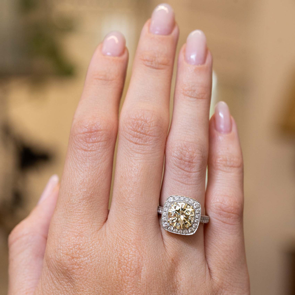 a hand held at distance wearing Vintage, 1990s yellow tinted diamond cluster engagement ring in white gold