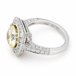 A white goldVintage, 1990s yellow tinted diamond cluster engagement ring against a white background at an angle to show off its diamond-set bezel 