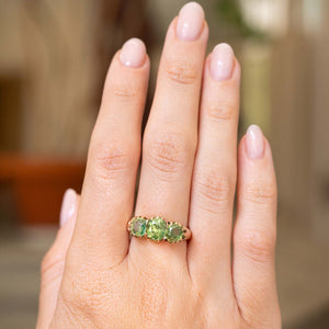 an image of a green zircon three-stone gold ring worn on the hand against a blurred background