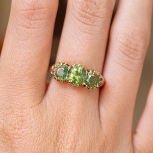 A close up picture of a green zircon trilogy ring in gold worn on the hand to show details.