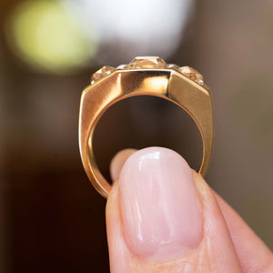 A close-up shot of a Vintage, 1970s Peruzzi cut diamond three-stone gypsy ring held between two fingers with a soft-focus background.