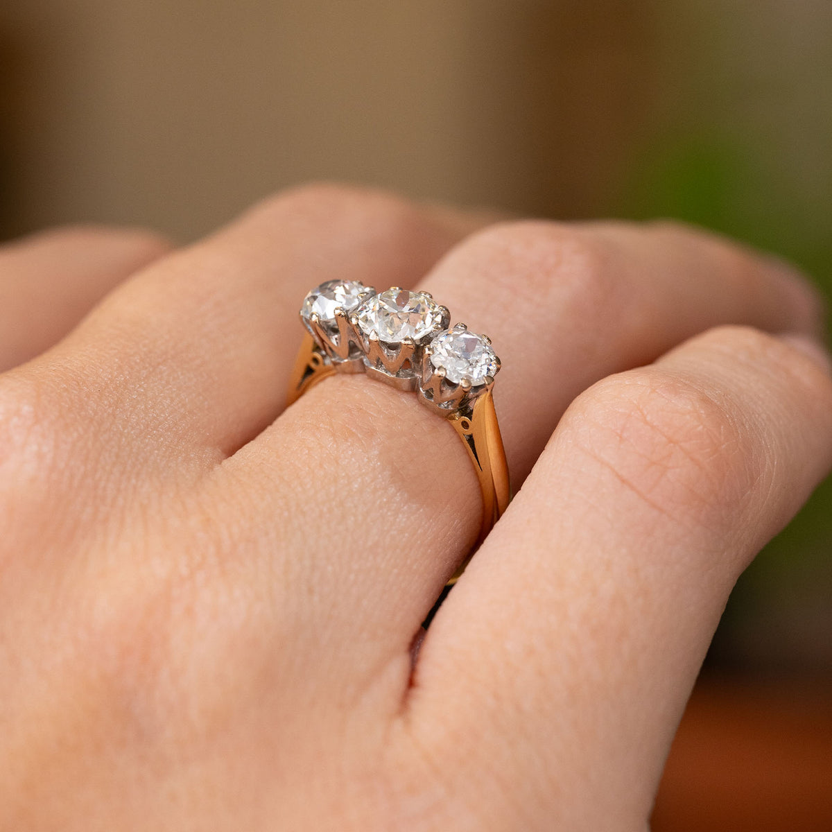 A close up image of a hand wearing a Vintage, 1990s old-cut diamond three-stone engagement ring in yellow gold shown from a side angle to show the profile of the ring.