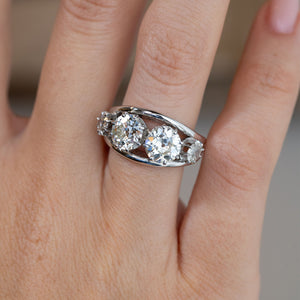 Close-up of the four-stone diamond engagement ring on a finger, featuring two prominent round old-cut diamonds in an openwork setting.