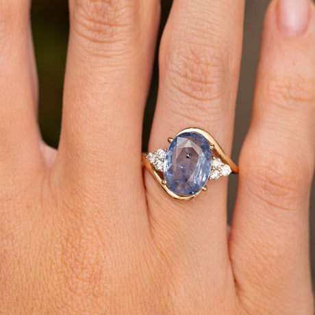 A close up detailed image of a hand wearing a Vintage, 1990s Blue sapphire and diamond trilogy yellow gold engagement ring