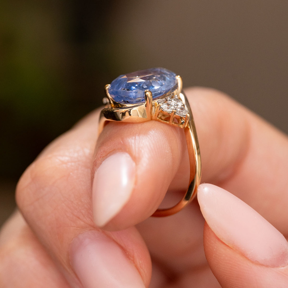 A hand wearing a Vintage, 1990s Blue sapphire and diamond three-stone ring in yellow gold showing off the profile of the ring against a blurred background