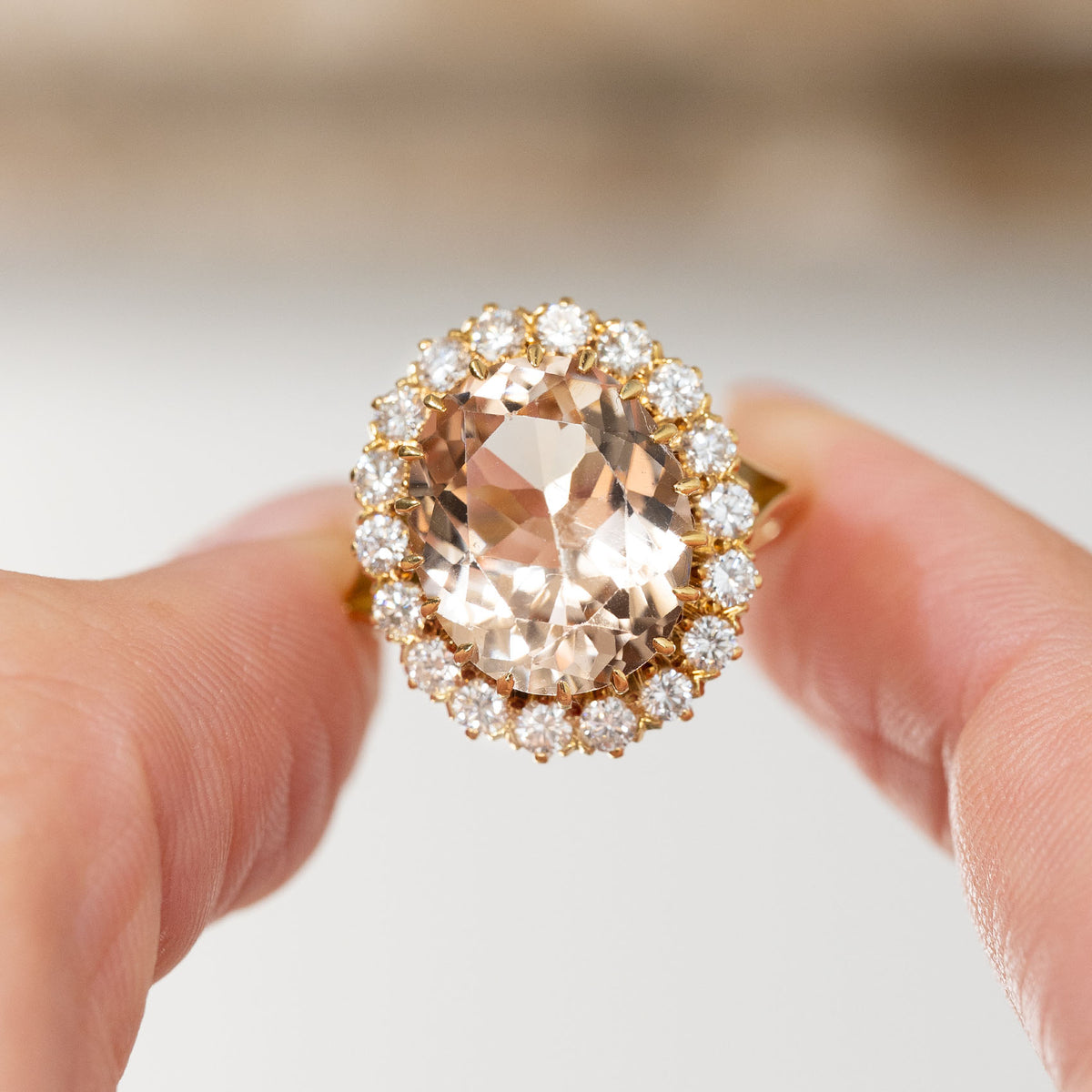 Handheld portrait of the oval topaz cluster ring, with a brilliant diamond halo framing the warm-toned gemstone.