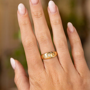  a hand wearing an antique a hand wearing an antique Edwardian era diamond trilogy gypsy ring on a thick yellow gold band with a high polish