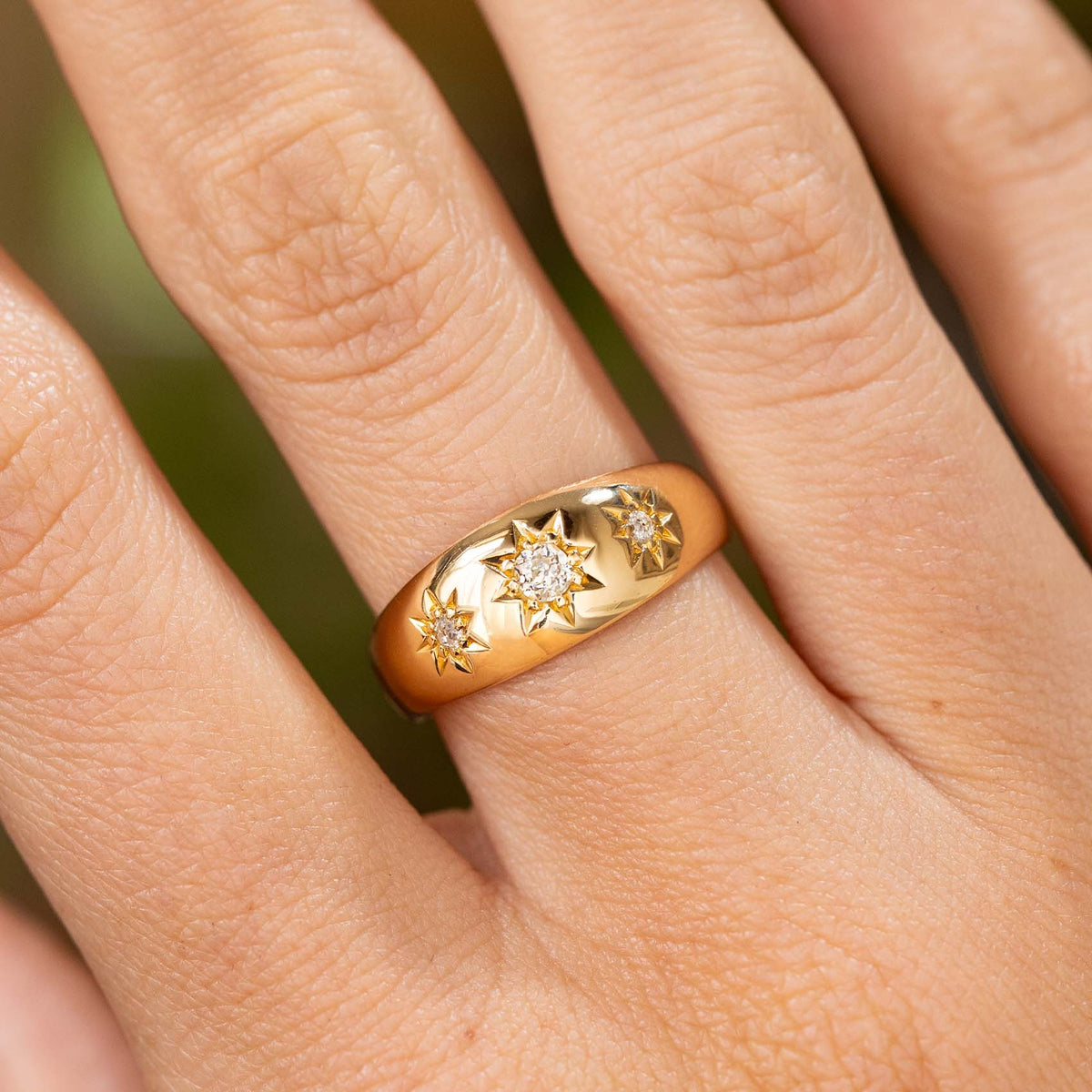An up close image of an antique Edwardian diamond three stone gypsy ring style with polished yellow gold and three old cut diamonds and engraved star settings