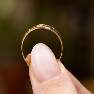  an antique Edwardian era gypsy ring with three old cut diamonds set in a yellow gold band held between the fingers and shown from the side to showcase the shank and the low an antique Edwardian era gypsy ring with three old cut diamonds set in a yellow gold band held between the fingers and shown from the side to showcase the shank and the low conforming profile of the ring