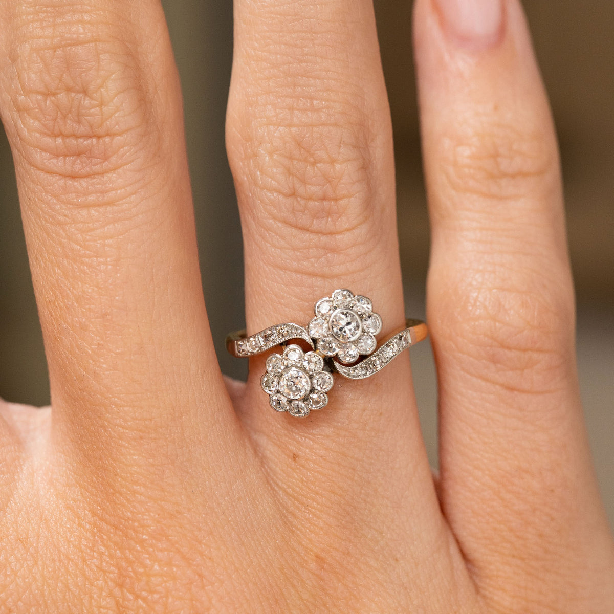 A close-up image of a finger that's wearing a yellow gold engagement ring formed of two old cut diamond clusters arranged as a toi et moi  shown off up close.