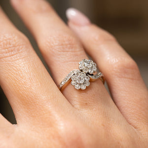 A close-up of a hand wearing an Antique, Edwardian diamond toi et moi engagement ring in yellow gold shown from a low angle to display the setting style and profile.
