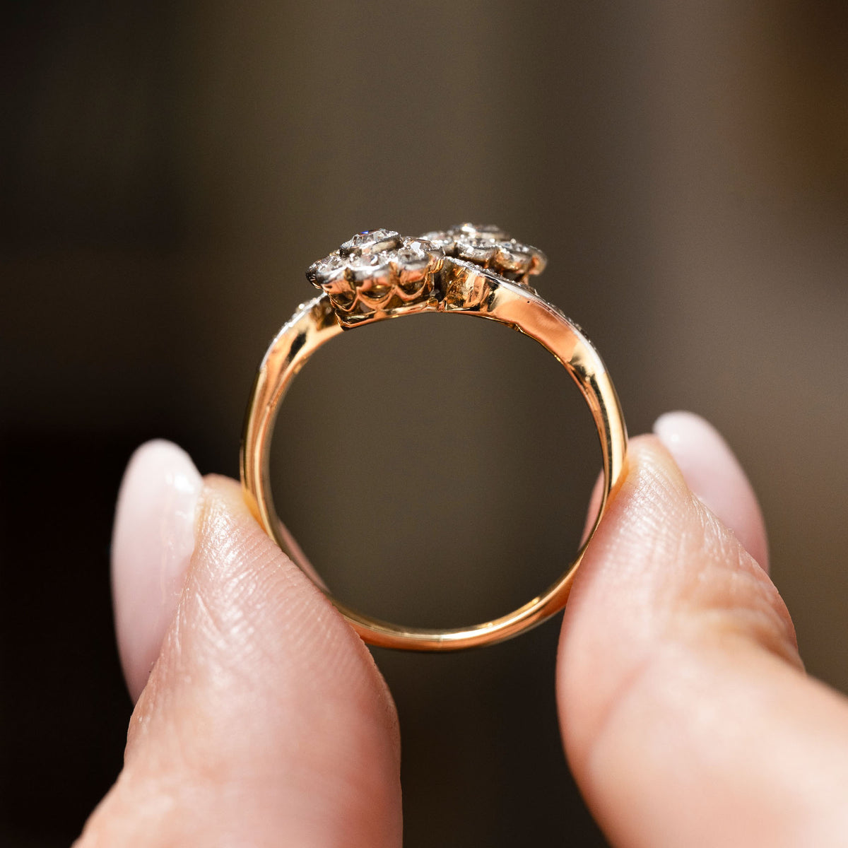 Antique, Edwardian diamond toi et moi engagement ring in yellow gold held in between two fingers up to the camera and from the side to display the shank and profile of the ring.
