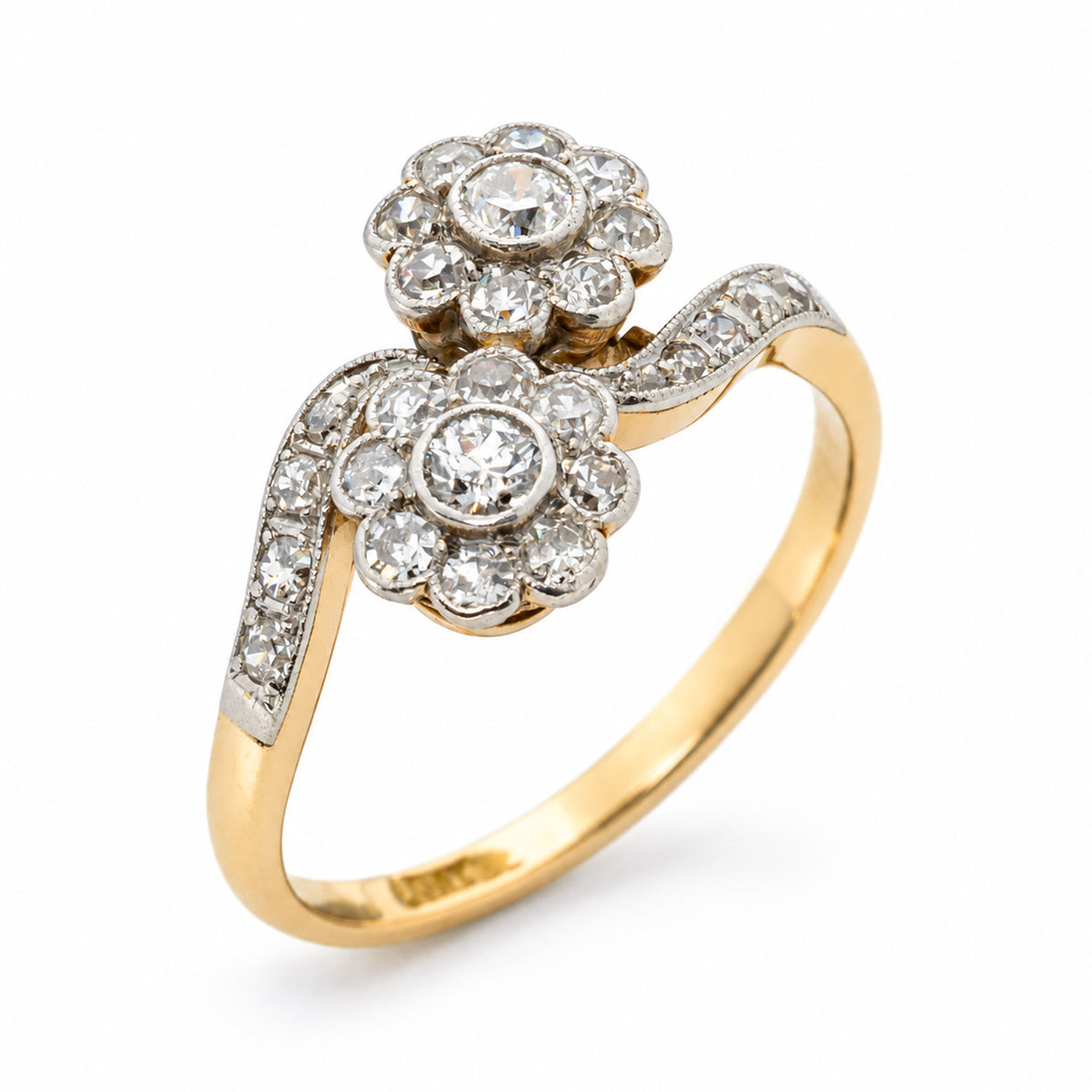  An antique Edwardian era engagement rang with two old cut diamond clusters in a crossover toi et moi arrangement on a yellow gold band against a plain white background at an angled position.