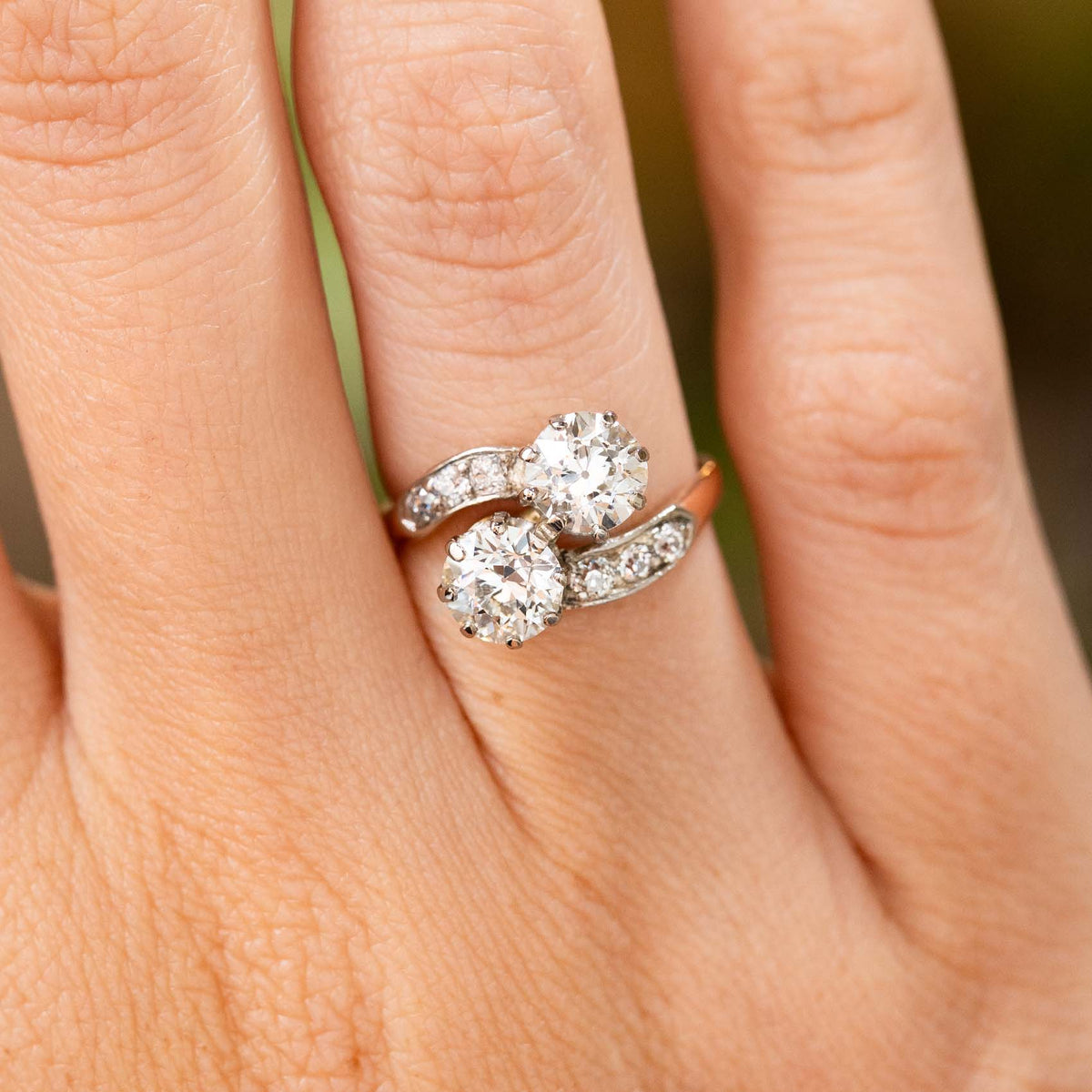 A close-up image of a hand wearing a yellow gold Antique, Edwardian diamond toi et moi engagement ring