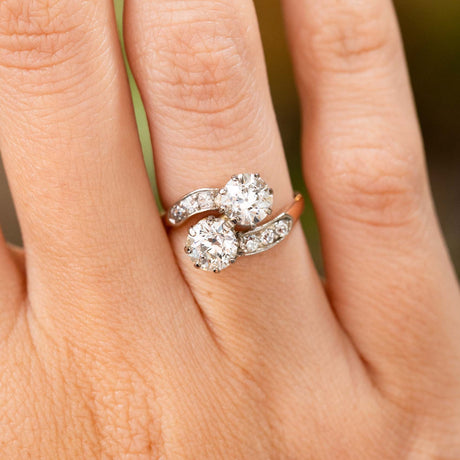 A close-up image of a hand wearing a yellow gold Antique, Edwardian diamond toi et moi engagement ring