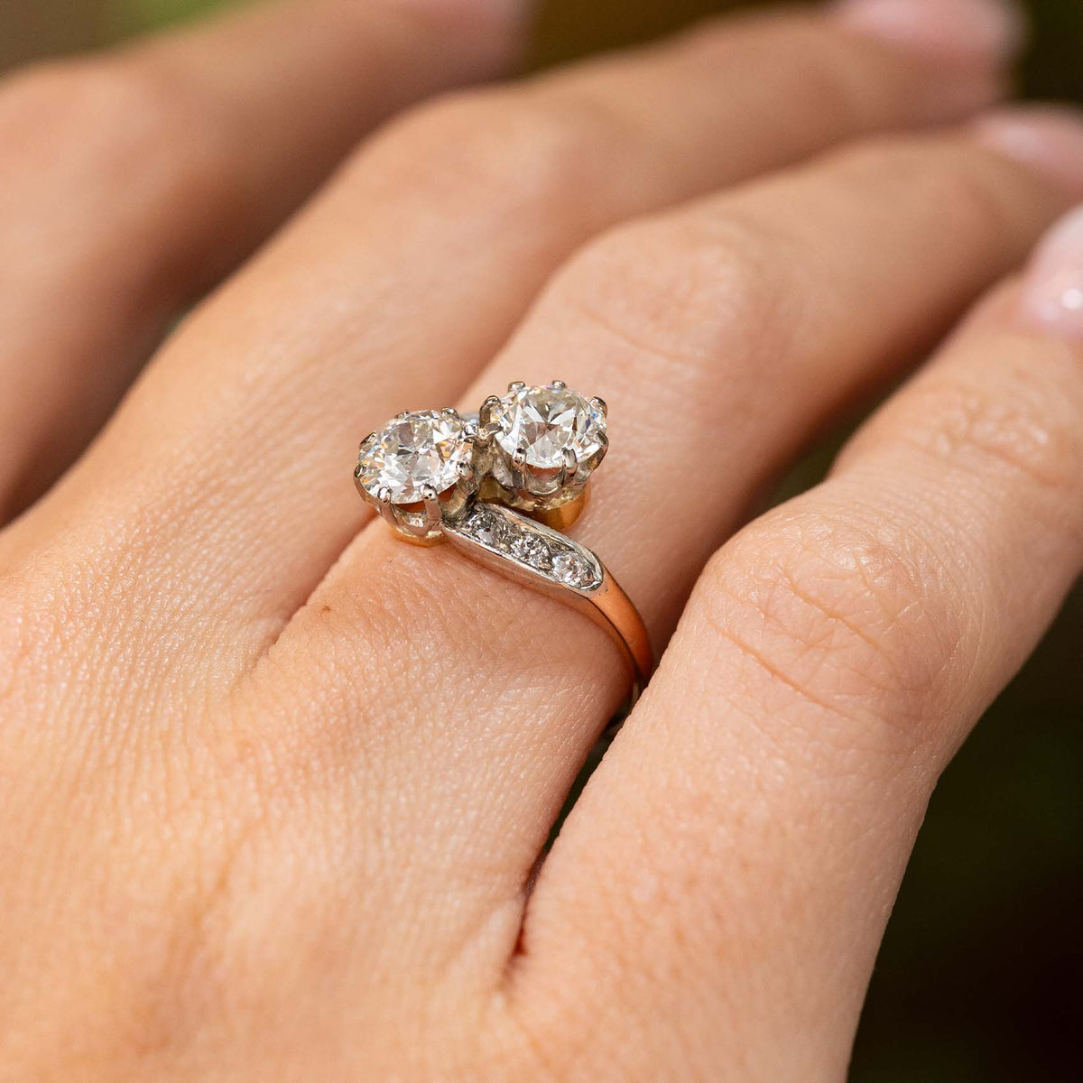  A hand wearing an antique Edwardian diamond two stone engagement ring in yellow gold pictured from a low angle close-up to show the profile of the ring.