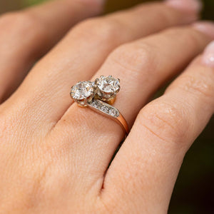  A hand wearing an antique Edwardian diamond two stone engagement ring in yellow gold pictured from a low angle close-up to show the profile of the ring.