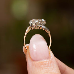  A close-up image of fingers holding Antique, Edwardian diamond toi et moi engagement ring in yellow gold held up to show the profile and shank of the Ring against a softly blurred background.