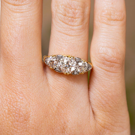 Close-up of an antique engagement ring worn, featuring three claw-set old-cut diamonds interspersed with tiny rose-cut diamonds.