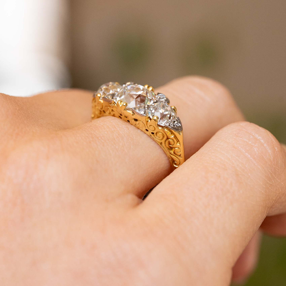 Side view of an antique Victorian ring worn, revealing the raised silver cut-down settings, scrolling gallery and engraved volute motifs along the gold shoulder.