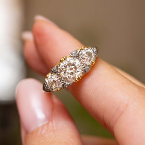 Angled close-up of the Victorian ring held between two fingers, showcasing the large cushion-shaped centre diamond and graduated old-cut side stones.
