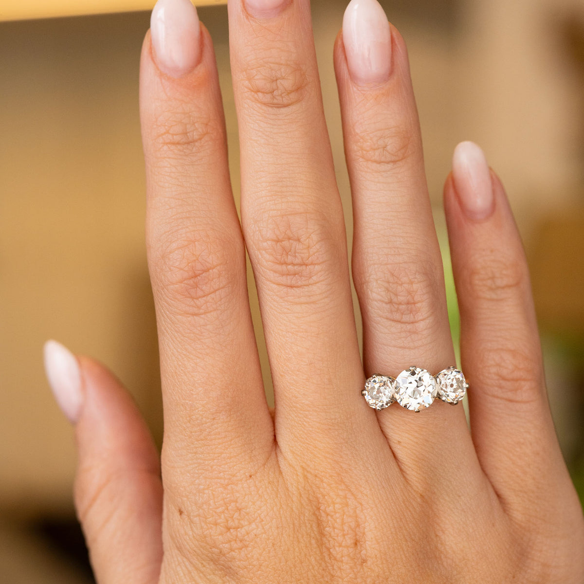 A hand wearing a platinum Antique, Edwardian old-cut diamond three-stone engagement ring.