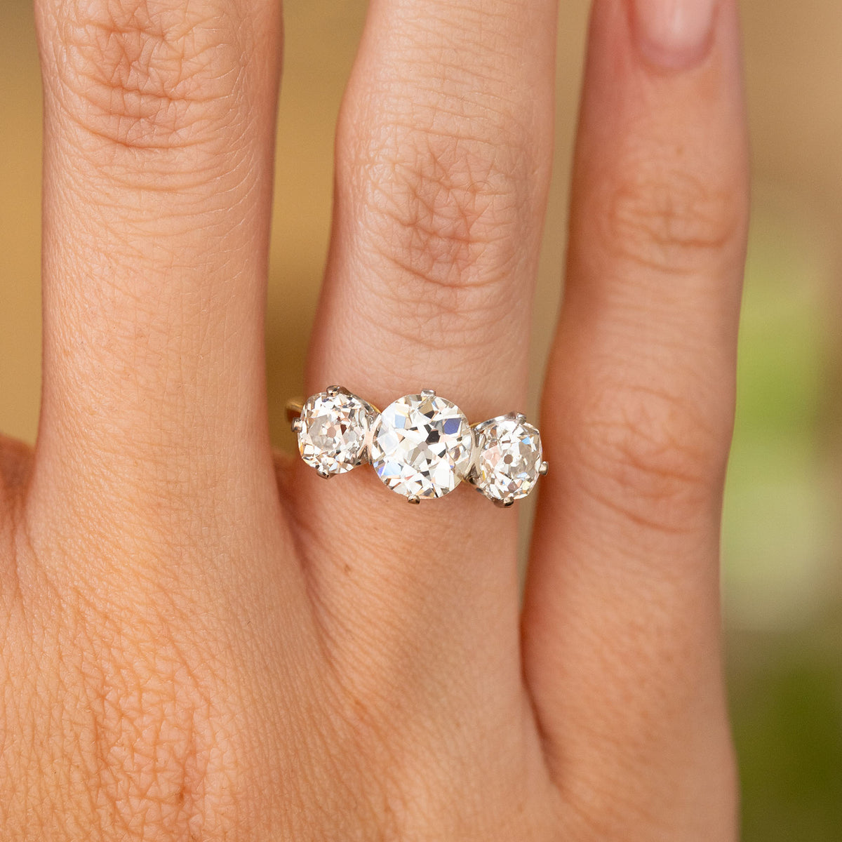A close-up image of an Antique, Edwardian old-cut diamond trilogy engagement ring with a yellow gold band being worn on the finger.