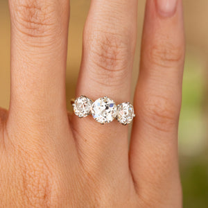 A close-up image of an Antique, Edwardian old-cut diamond trilogy engagement ring with a yellow gold band being worn on the finger.