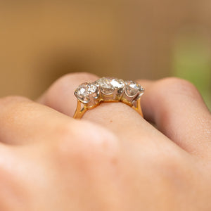 A close-up image of an Antique, Edwardian old-cut diamond three-stone engagement ring with platinum settings and a yellow gold band being worn on the finger and shown up close from a low angle to display the setting and profile