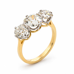 Antique, Edwardian old-cut diamond trilogy engagement ring on a yellow gold band at an upright angle against a plain white background