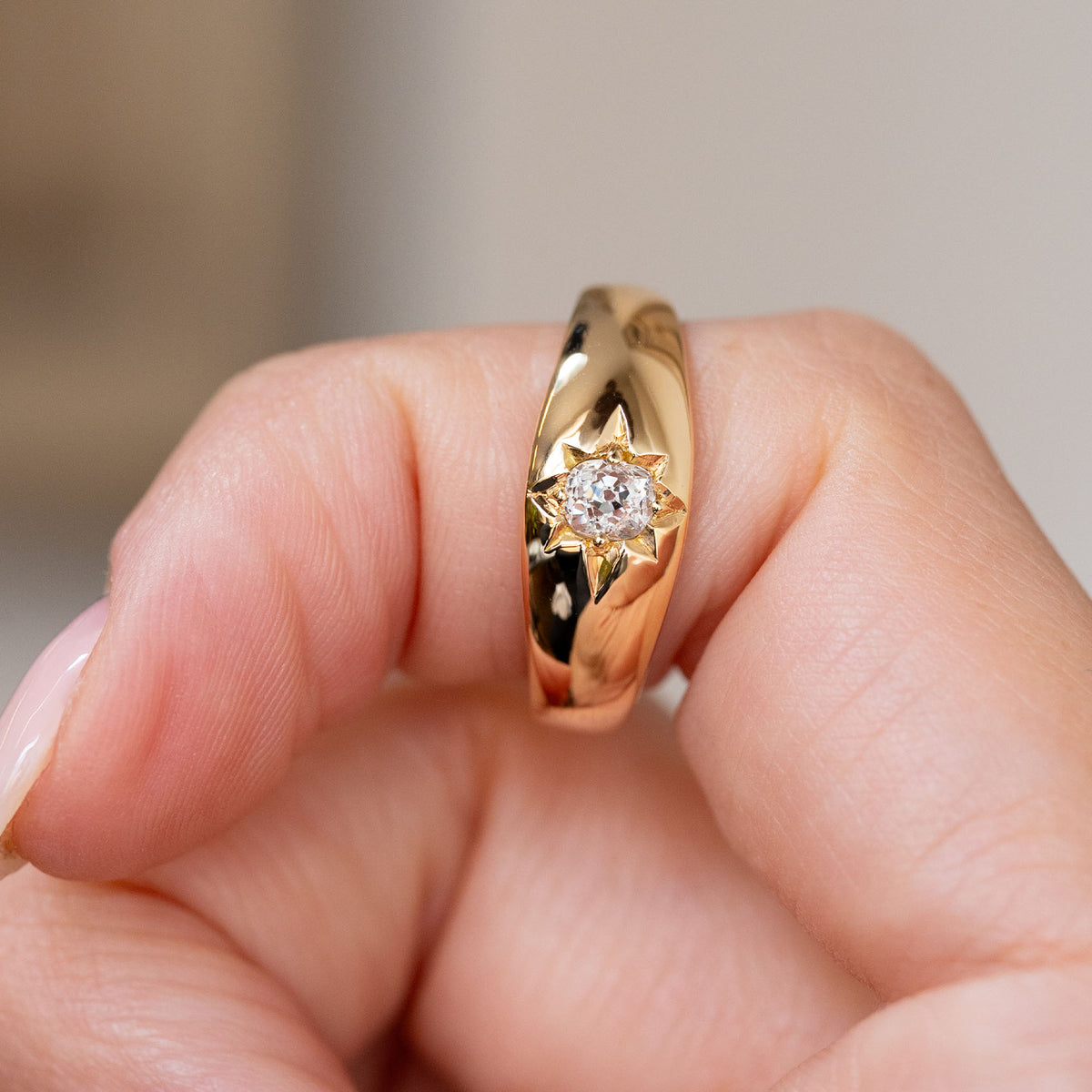 Victorian yellow gold gypsy ring held between the fingers, revealing its smoothly domed and tapered profile.