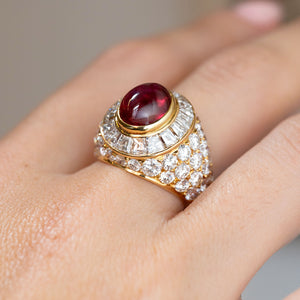 Side angle on the hand showing the raised cabochon ruby, concentric diamond surround and rounded bombé silhouette.