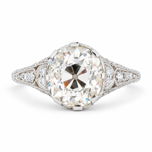 Antique Edwardian old-mine cut diamond solitaire engagement ring with diamond-set shoulders and delicate milgrain detailing.