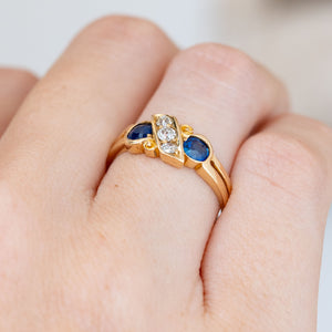 Seen obliquely, the antique ring reveals its split shoulders, raised gemstones and flowing scrollwork around the five-stone setting.
