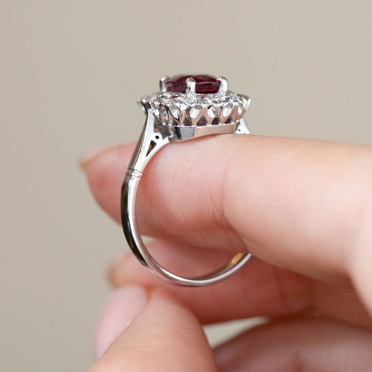 Side profile of the vintage ruby ring held between fingers, revealing the openwork gallery, elevated diamond setting and polished white gold shank.