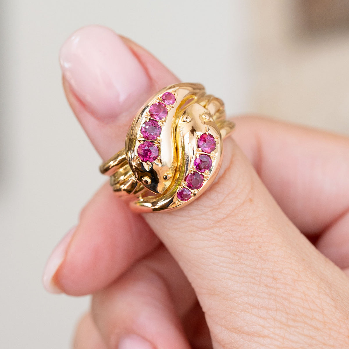 Antique yellow gold snake ring held between the fingers, capturing the sculpted heads and rich ruby colour.