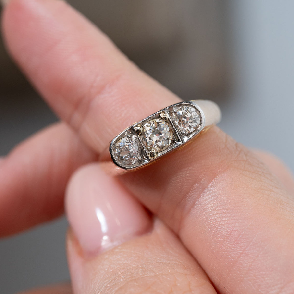Detailed close-up of an antique Edwardian diamond three-stone ring held between fingers, highlighting the central old-cut diamond flanked by two smaller diamonds in a platinum setting.