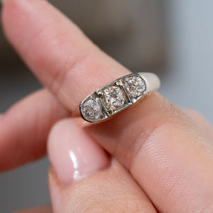 Detailed close-up of an antique Edwardian diamond three-stone ring held between fingers, highlighting the central old-cut diamond flanked by two smaller diamonds in a platinum setting.