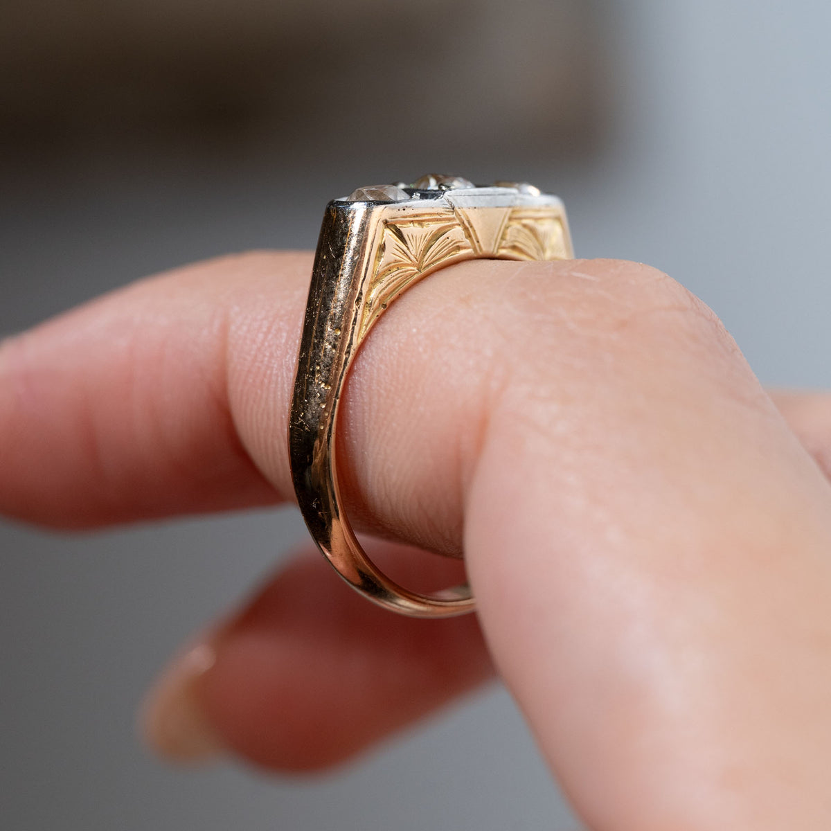 Side profile of an antique Edwardian diamond three-stone engagement ring held between fingers, showing the engraved yellow gold shoulders, intricate detailing and raised platinum diamond setting.