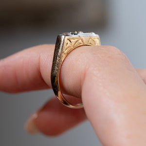 Side profile of an antique Edwardian diamond three-stone engagement ring held between fingers, showing the engraved yellow gold shoulders, intricate detailing and raised platinum diamond setting.