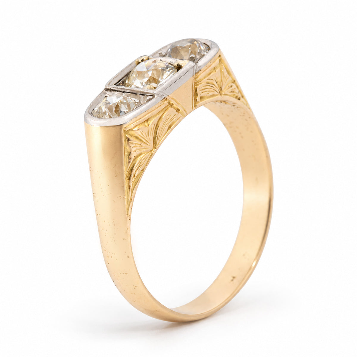 Angled view of an antique Edwardian diamond three-stone ring, showcasing its old-cut diamonds, platinum setting and intricately engraved yellow gold shoulders.