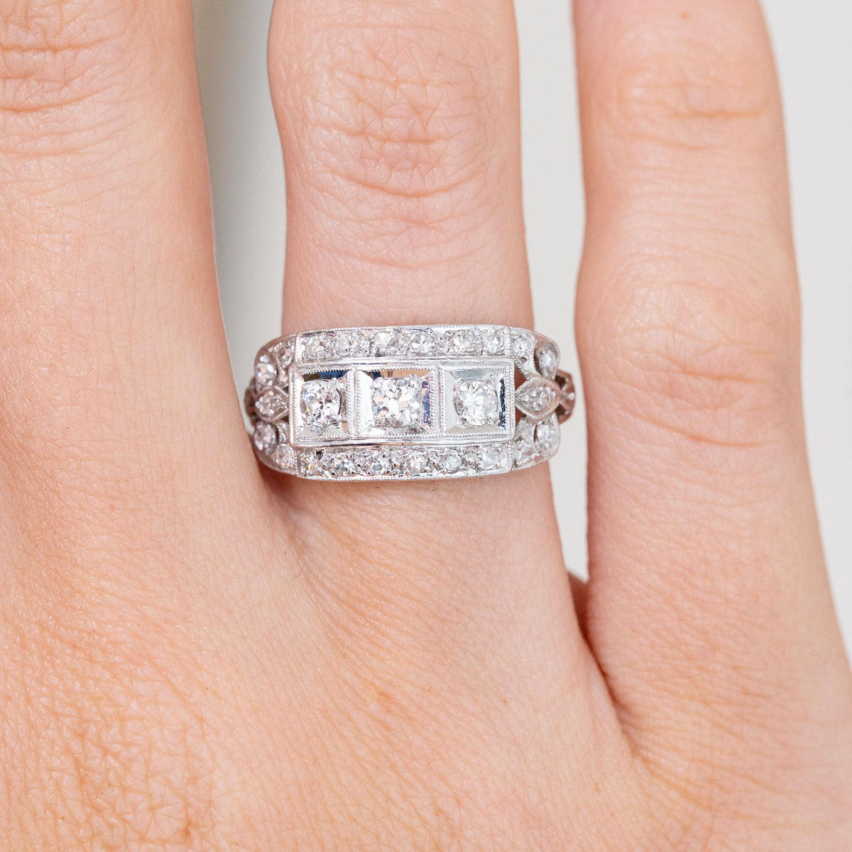 Close-up on-hand view of the platinum ring, revealing three prominent diamonds surrounded by rows of smaller stones.