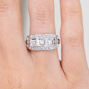 Close-up on-hand view of the platinum ring, revealing three prominent diamonds surrounded by rows of smaller stones.