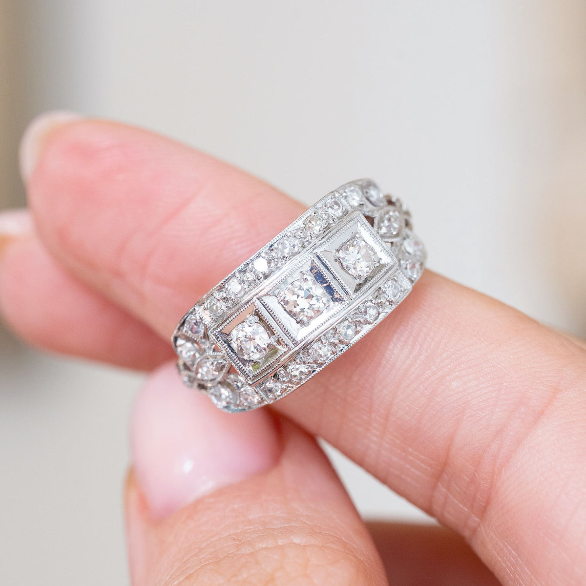Platinum diamond cluster ring held between the fingers, offering a detailed look at its intricate vintage craftsmanship.
