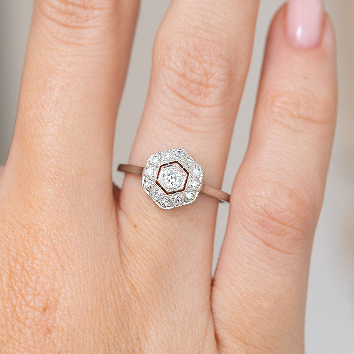 Close-up on-hand view of the white gold and platinum ring, featuring a central diamond within a hexagonal diamond surround.
