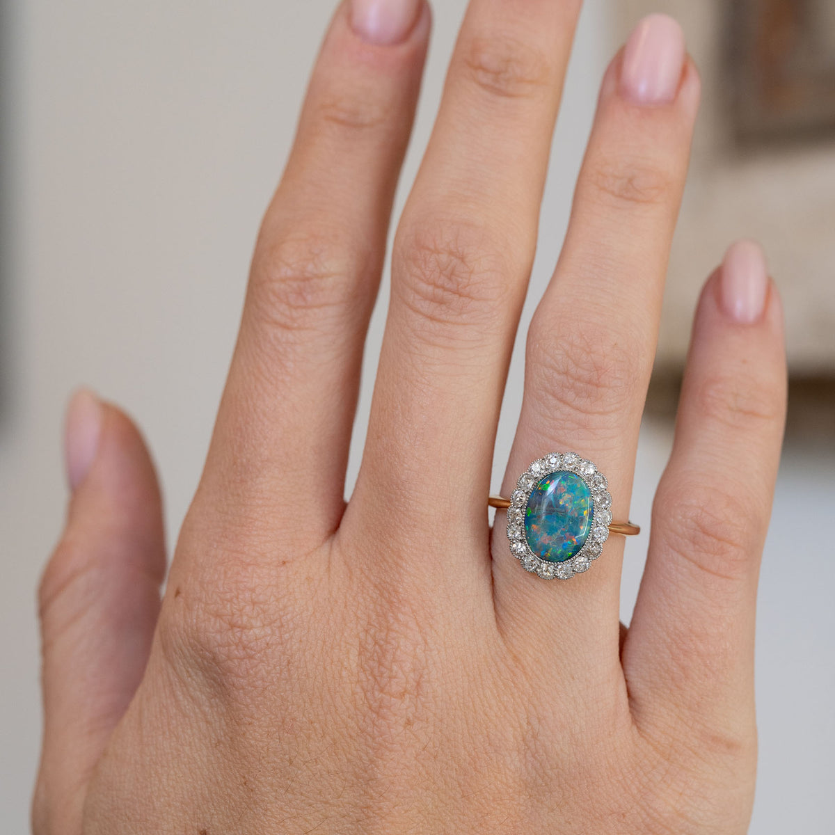Antique black opal cluster ring worn on the hand, displaying its vibrant colour flashes and elegant platinum-set diamond surround.