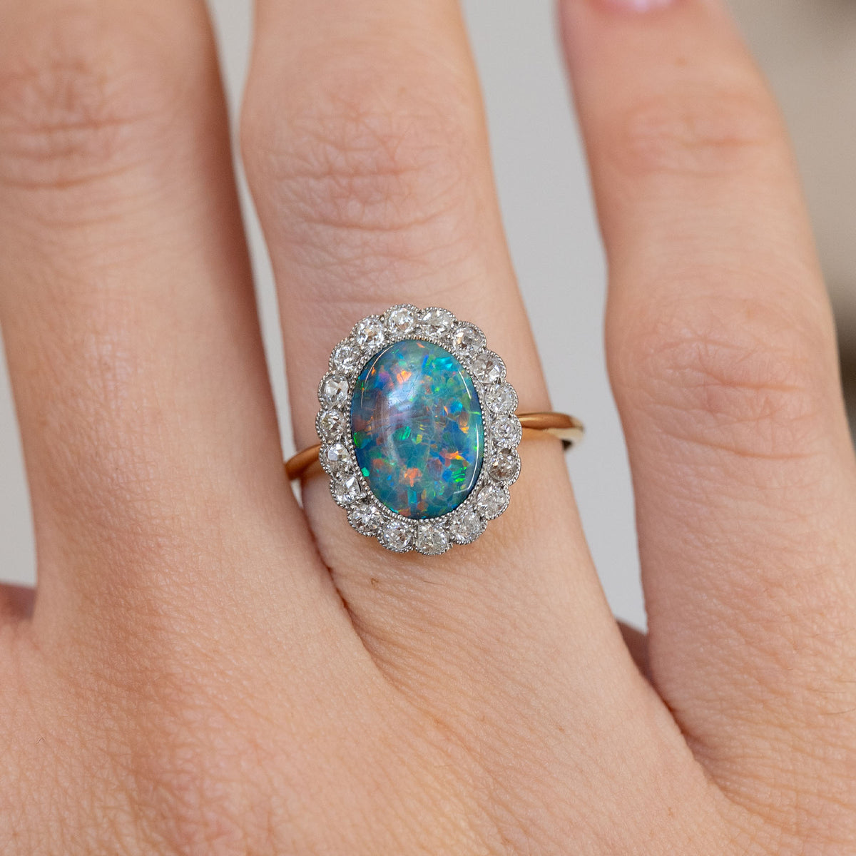 Close hand detail highlighting the multicoloured oval black opal and sparkling floral-style diamond cluster.