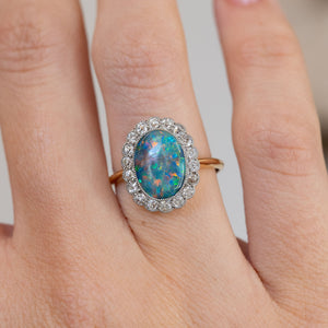 Close hand detail highlighting the multicoloured oval black opal and sparkling floral-style diamond cluster.