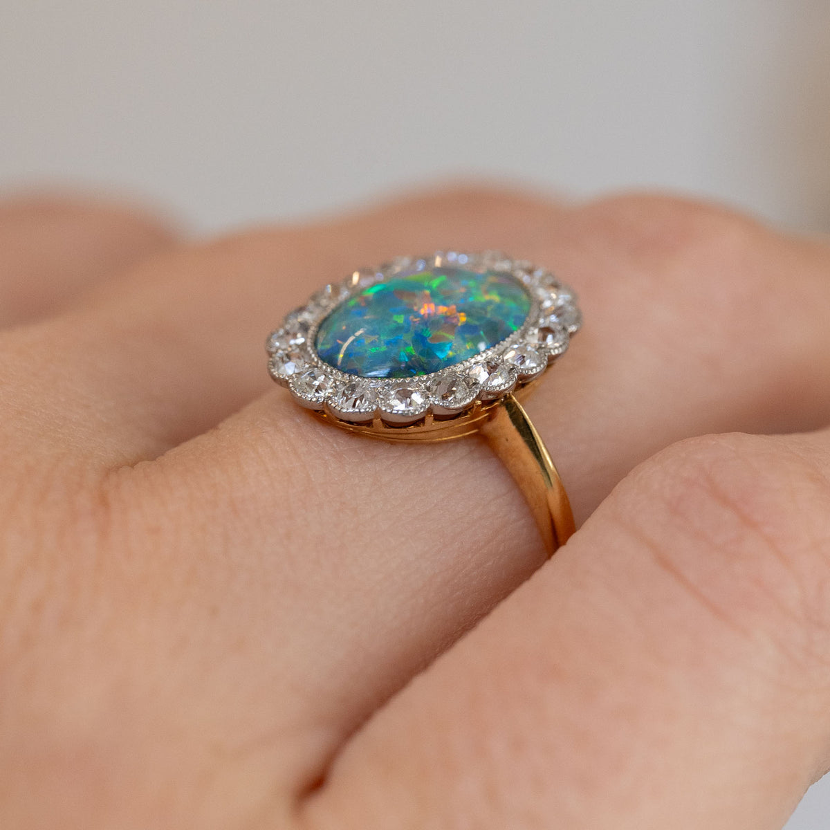 Low angled view of the Edwardian ring being worn, revealing its raised platinum cluster setting and slender yellow gold band.